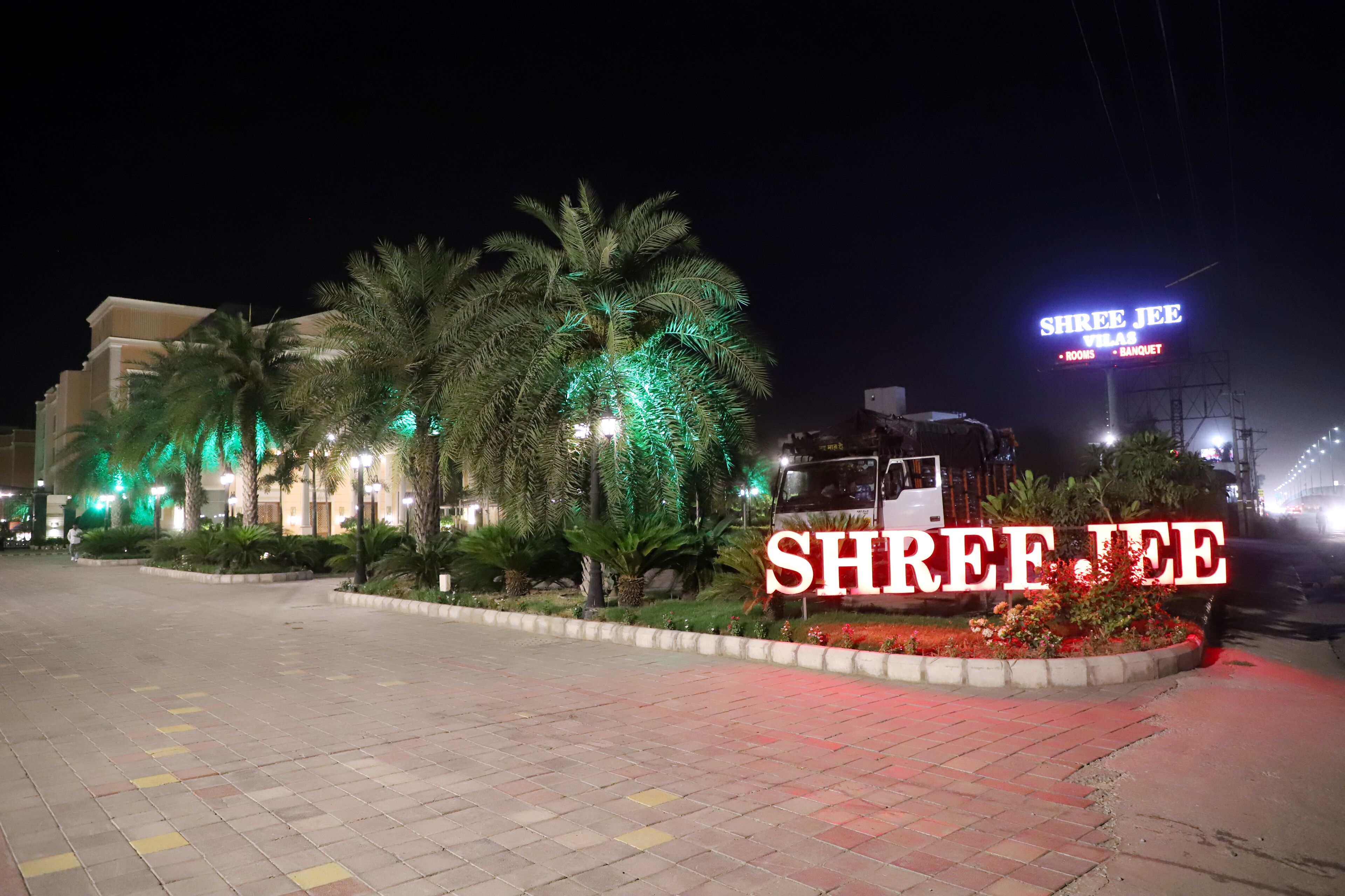 A hotel entrance with a sign reading "Shree Jhee Villa - Banquet" and a well-lit palm tree area.