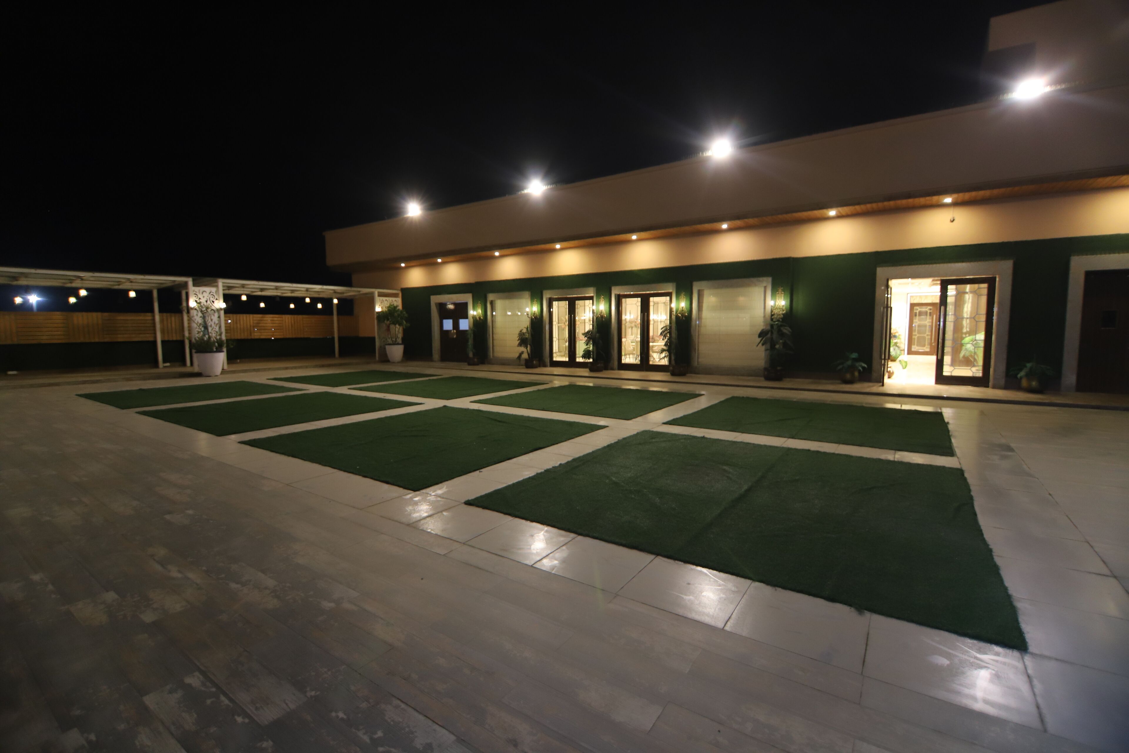 L’extérieur d’un hôtel de nuit, avec un espace extérieur couvert, un sol carrelé et une section de gazon artificiel vert.