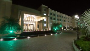 Una entrada de hotel con un corredor cubierto, palmeras y un sendero bien iluminado.