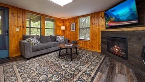 A cozy living room with a fireplace, a large TV, and a patterned rug.