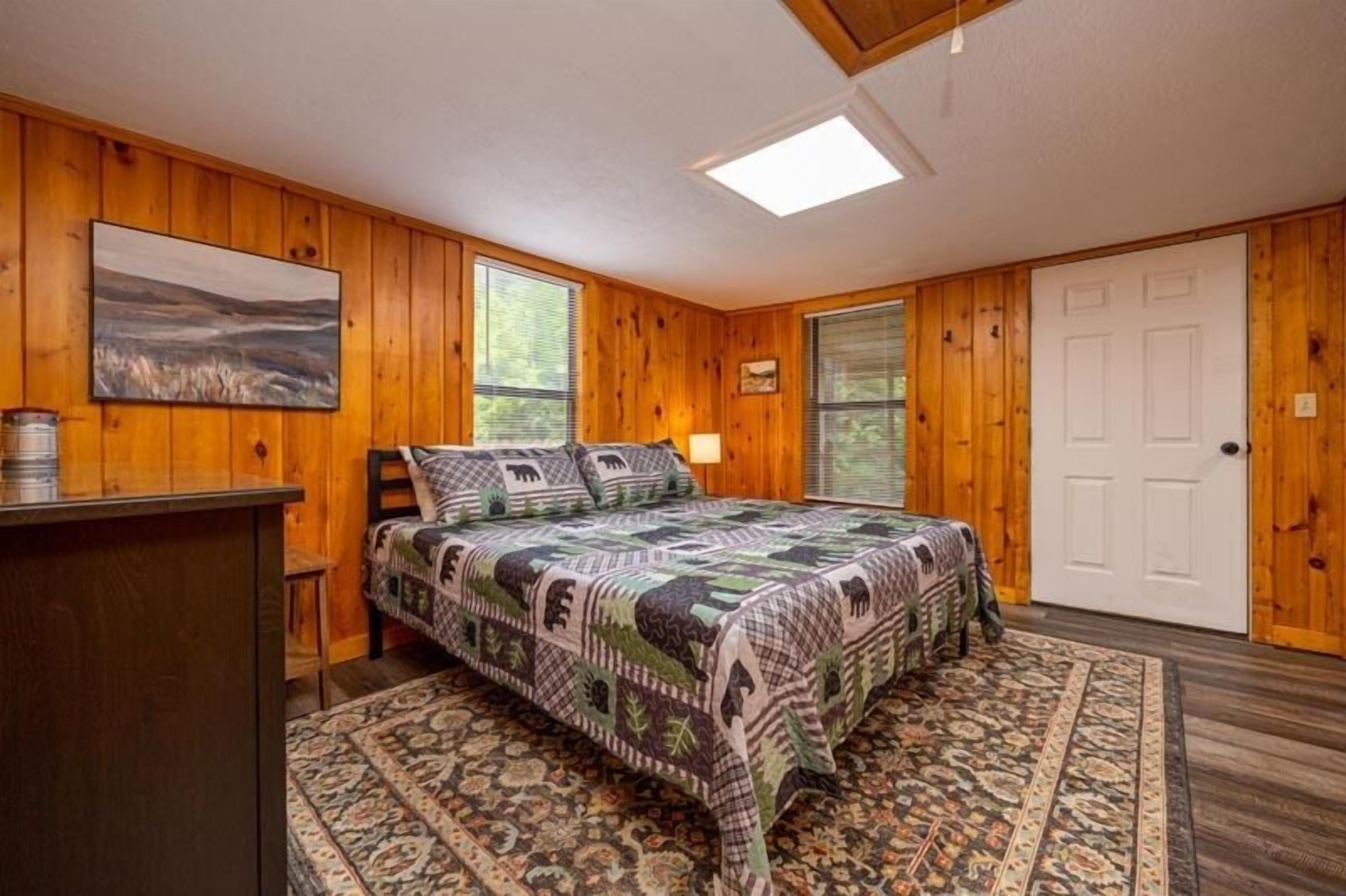 A bedroom with wooden walls, a bed with patterned bedding, a desk, and a rug.