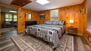 A bedroom with a bed, a nightstand, a lamp, a dresser, and a window.