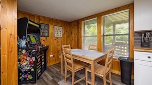 A room with a wooden interior, a table with chairs, a window with blinds, and a kitchen area with cabinets and a sink.