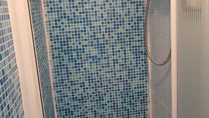 A shower area with blue mosaic tiles and a glass door.