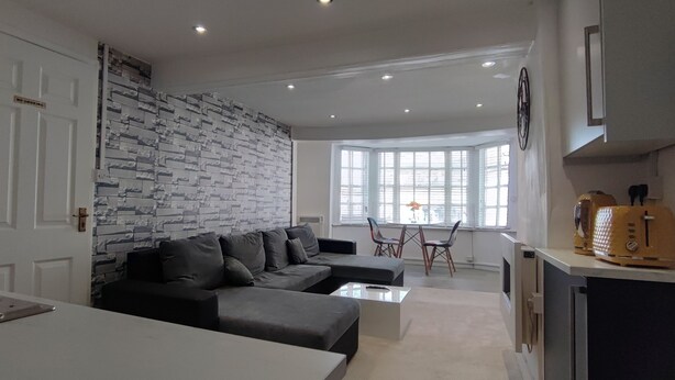 A modern living room with a grey sofa, a white coffee table, and a kitchen area with a stove and a yellow appliance.