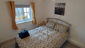 A bedroom with a bed, a window with curtains, a radiator, and a cityscape artwork on the wall.