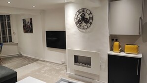 A modern living room with a flat-screen TV, a decorative clock, a fireplace, and a yellow kettle on a cabinet.