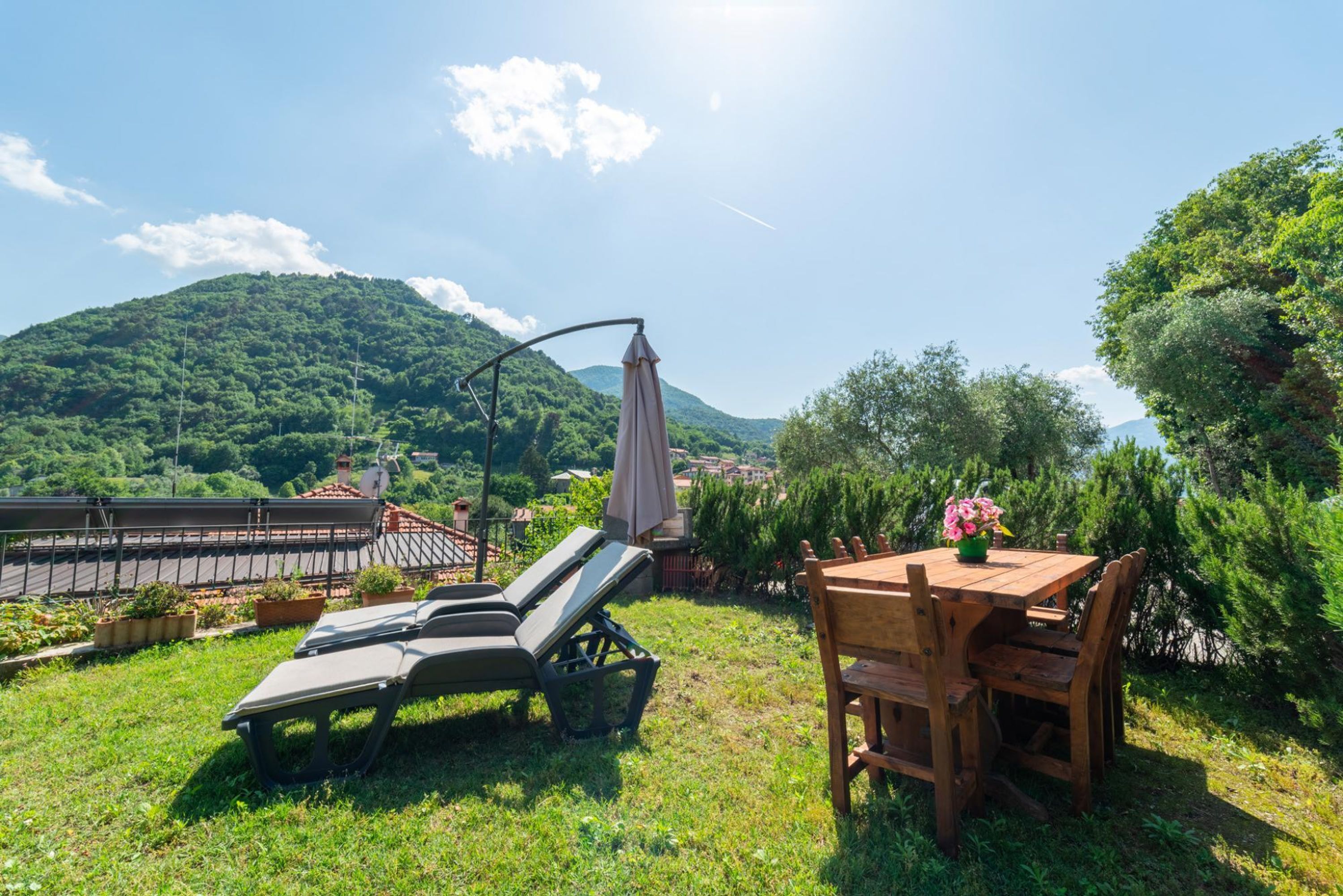 Une terrasse avec une table et des chaises, un transat et une vue sur une montagne.