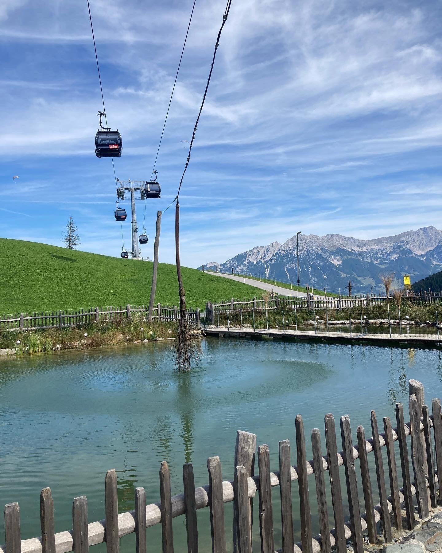A lake with a wooden fence, a cable car system, and mountains in the background.