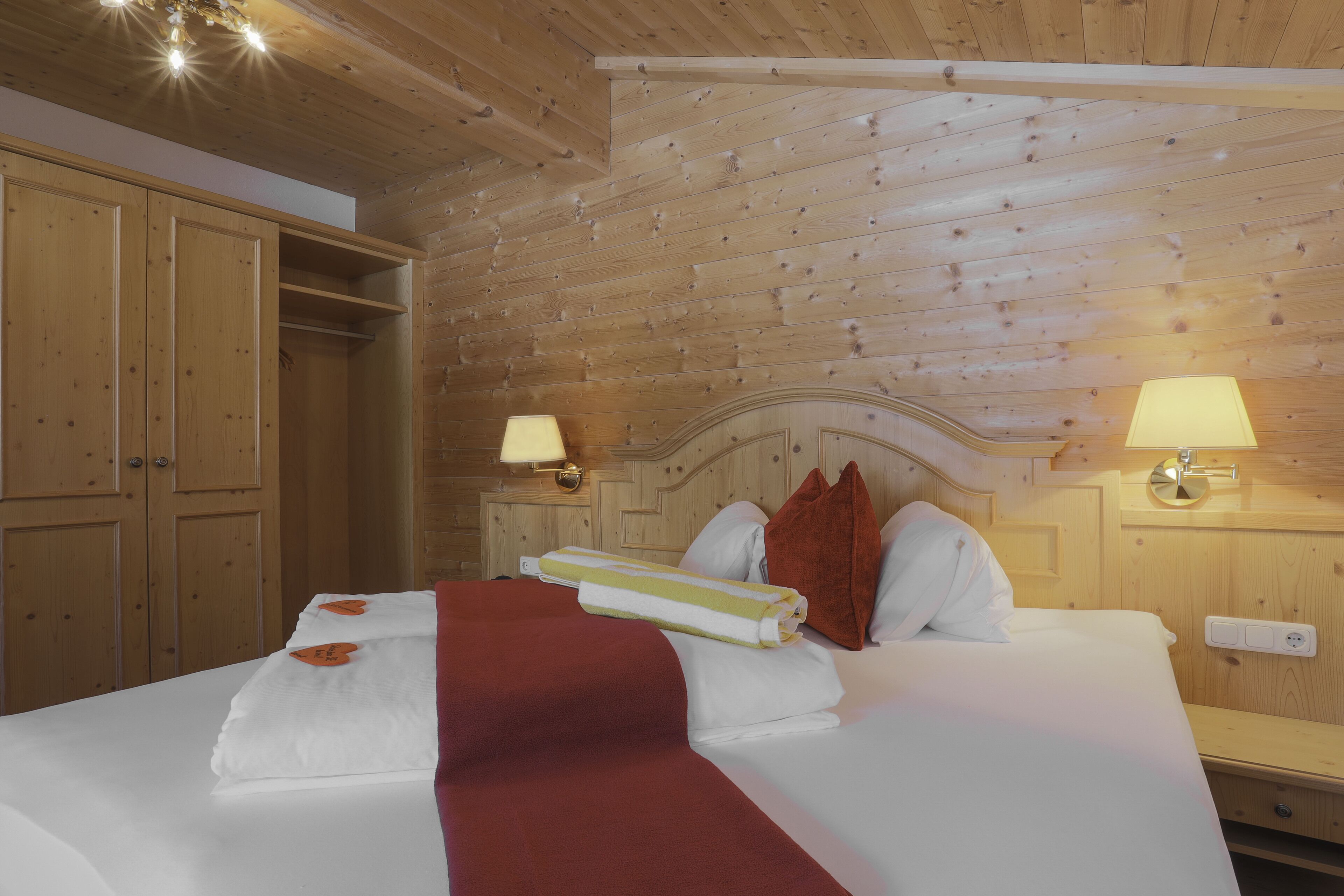 A wooden-paneled room with a bed, two bedside lamps, and a nightstand.