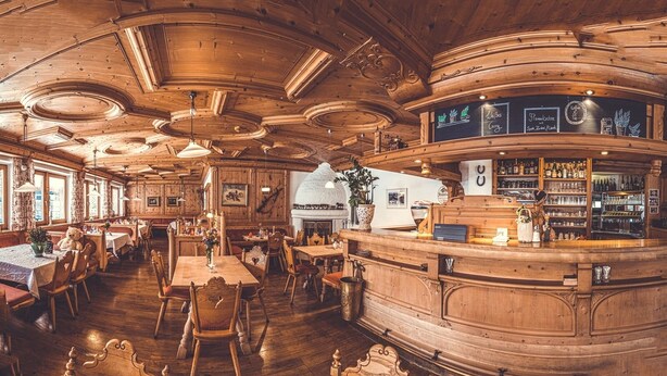 Un interior de madera con mesas y sillas redondas, una zona de bar y un menú en una pizarra.