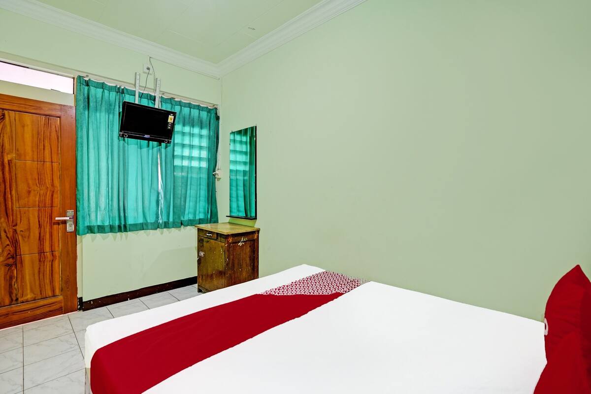 Un dormitorio con una cama, un armario de madera, una mesita pequeña y un televisor montado en la pared.