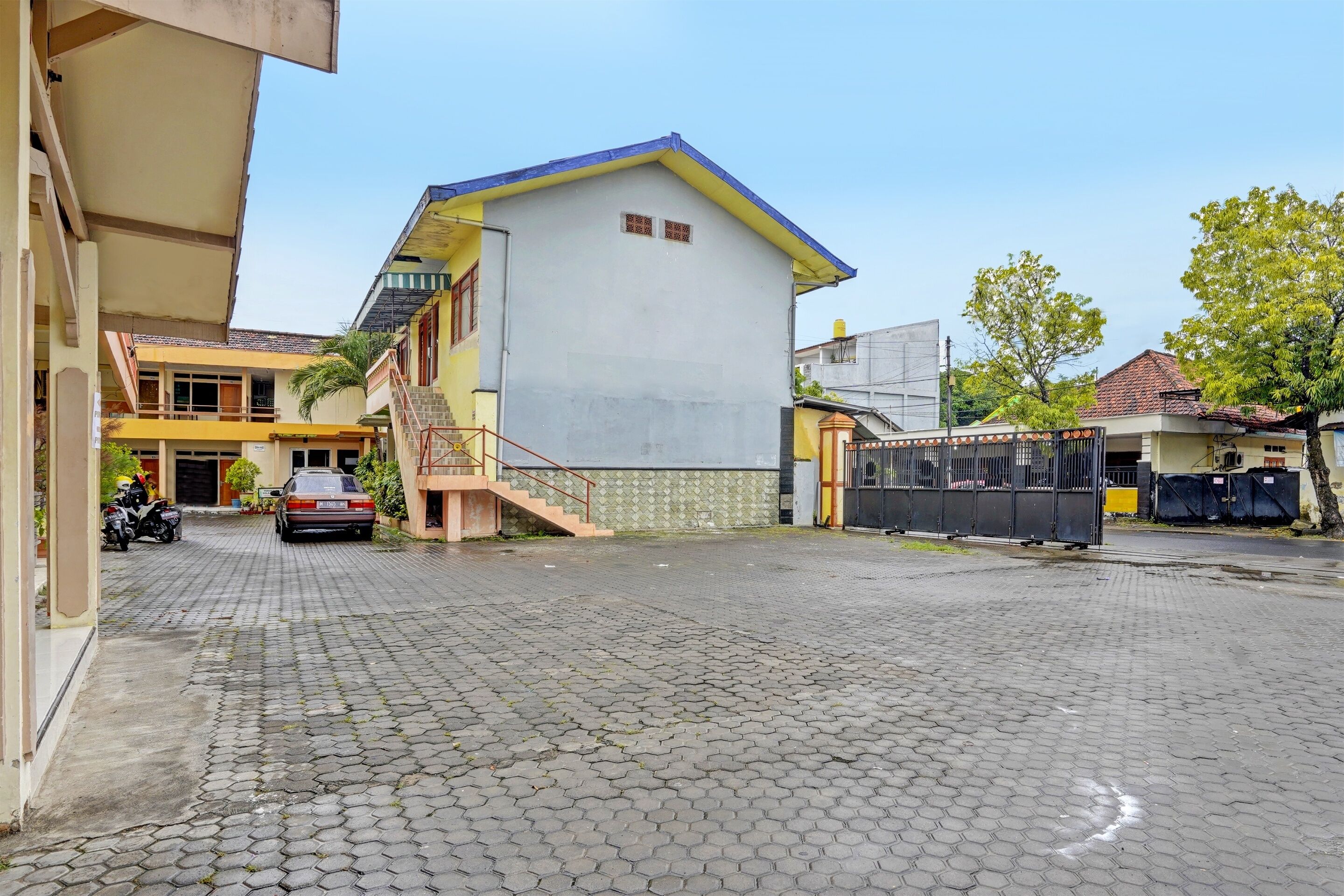 Ein Gebäude mit einer Treppe, die zu einer Tür führt, ein geparktes Auto und einem gepflasterten Innenhof.