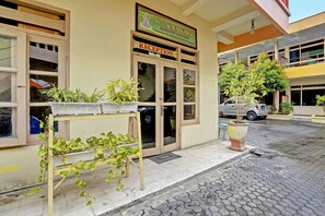 Un hall d’hôtel avec une enseigne au-dessus de la porte, des plantes en pot et une voiture garée.