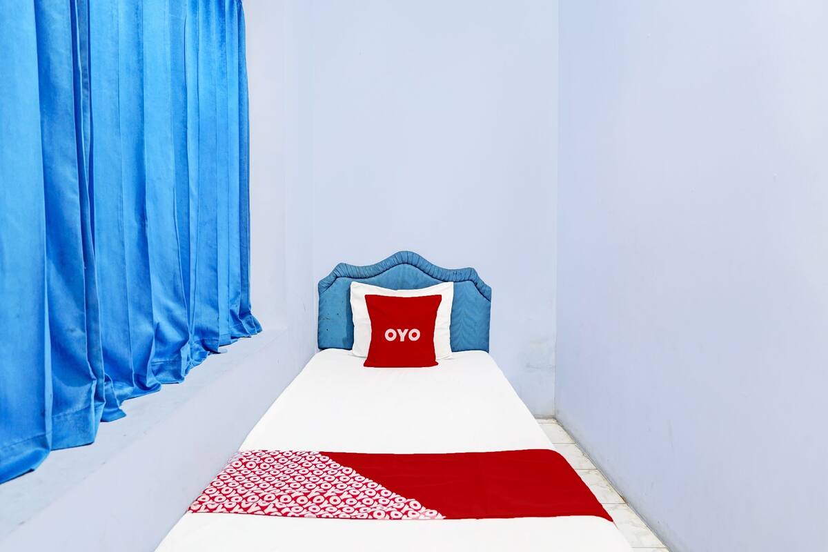 Una habitación estrecha con una cama, una cortina azul y un cojín rojo con la palabra 