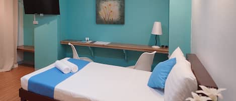A hotel room with a bed, a desk, a chair, a TV, and a painting on the wall.