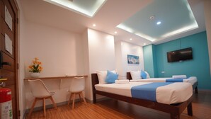 A modern hotel room with a wooden floor, a desk with a chair, a bed with blue bedding, a TV on the wall, and a painting above the bed. - ARZO Hotel Premier (Makati)