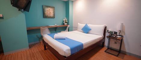 A modern hotel room with a wooden bed, a desk, and a TV mounted on the wall.
