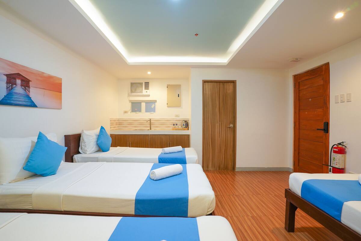 Ein Hotelzimmer mit zwei Betten, einer Holztür, einem Feuerlöscher und einem Gemälde an der Wand.