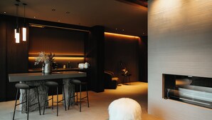 A modern kitchen with a bar area, a fireplace, and a fluffy white dog on a rug. - Signature by Vík Apartments (Vik I Myrdal)
