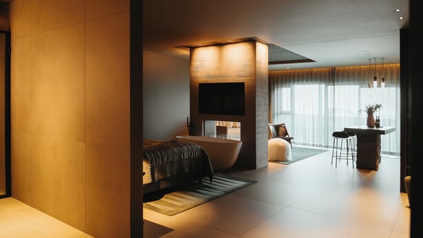 A modern bedroom with a large bed, a bathtub, and a dining area with a table and chairs. - Signature by Vík Apartments (Vik I Myrdal)