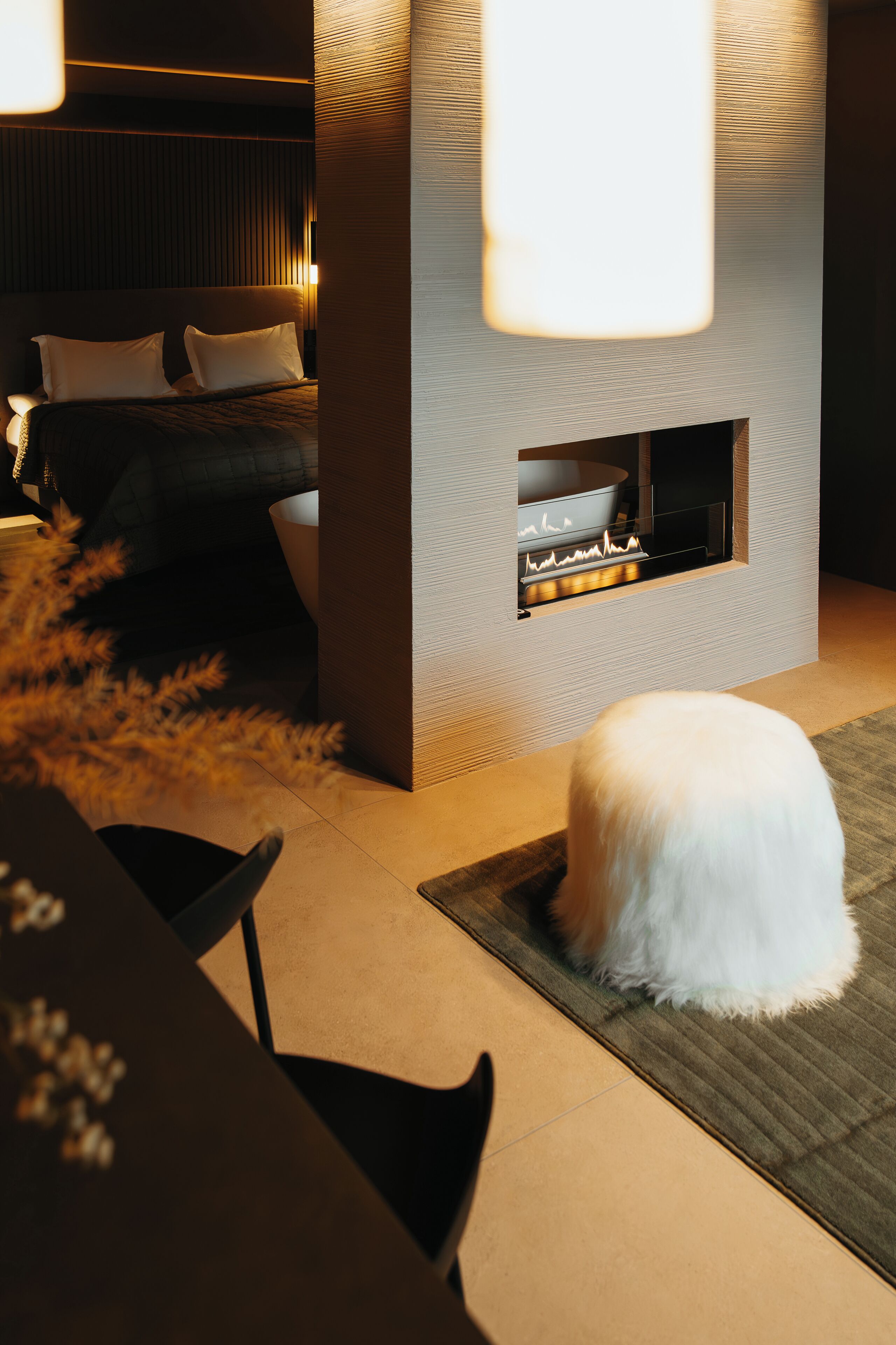 A modern room with a bed, a fireplace, and a white fluffy rug.