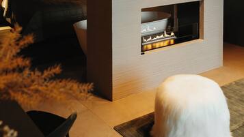 A modern room with a bed, a fireplace, and a white fluffy rug.