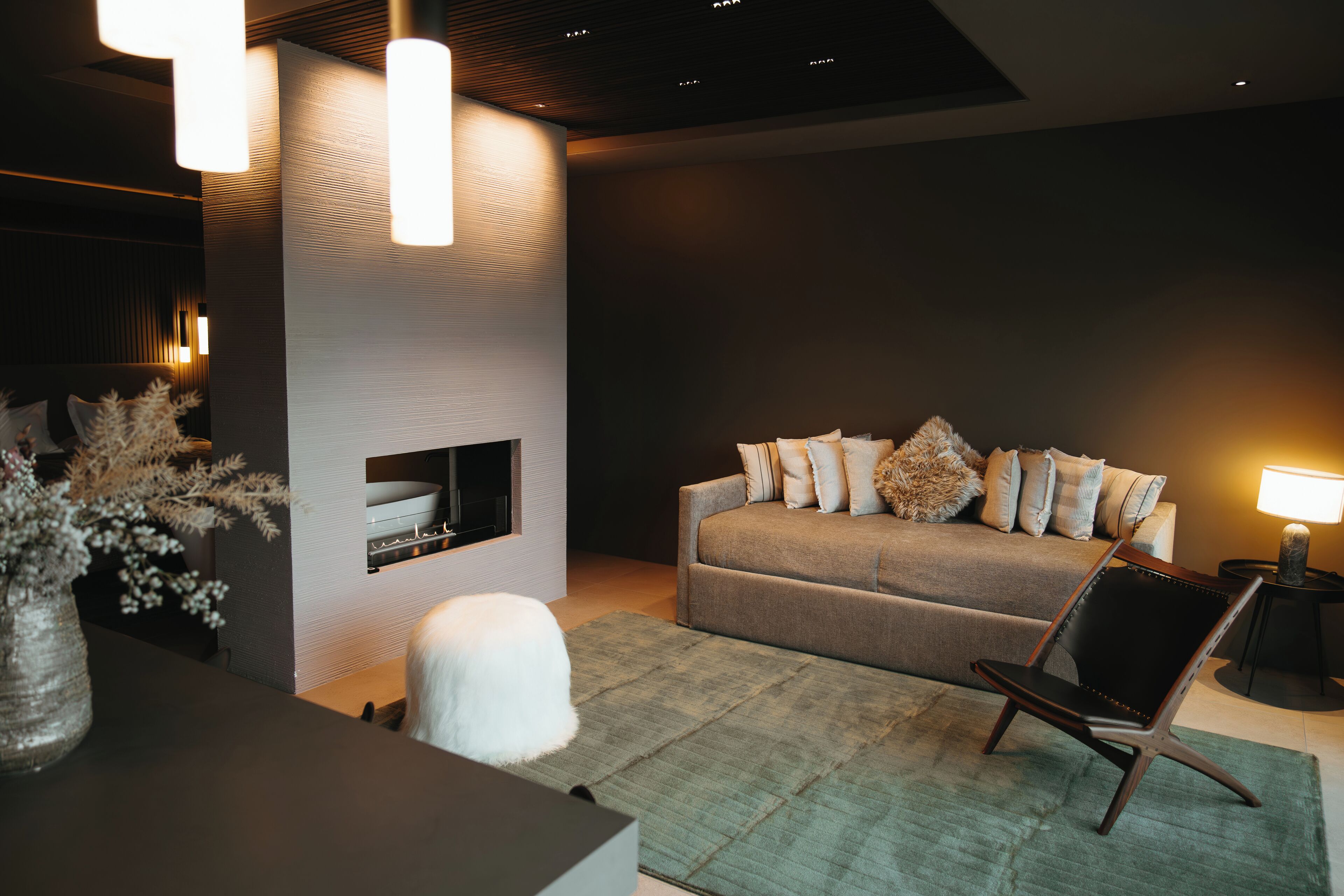 A modern living room with a sofa, a chair, a fireplace, and pendant lighting.