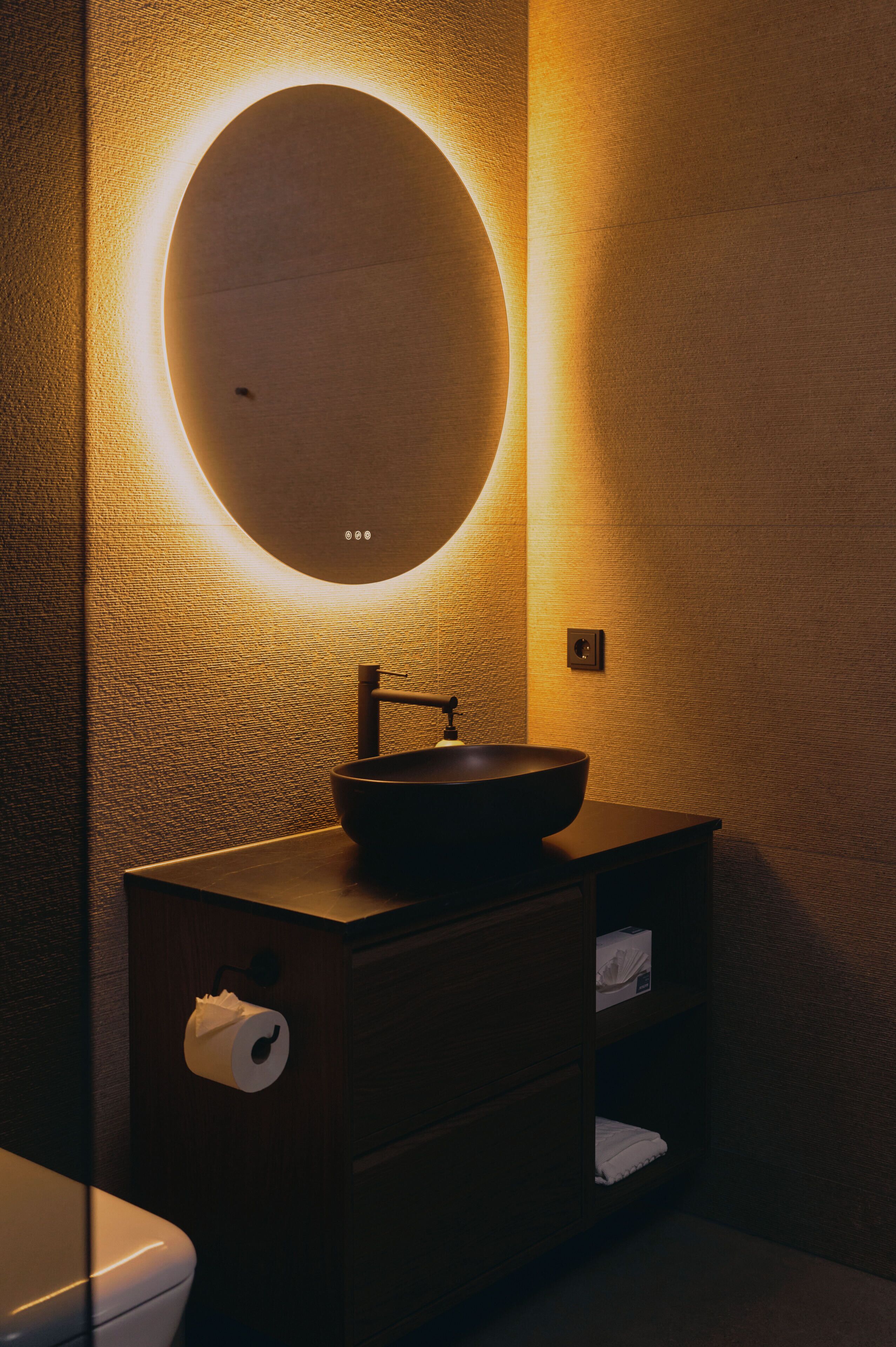 Un baño con un espejo redondo, un lavabo, un inodoro y un dispensador de pañuelos.