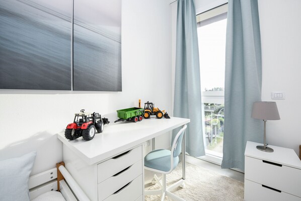 A child's room with a white desk, a chair, a bed, and a window with curtains.