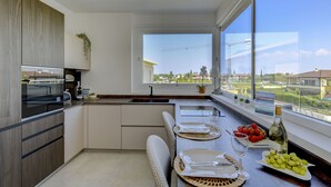 Eine moderne Küche mit einem großen Fenster, einer Essecke mit gedecktem Tisch für zwei Personen und Blick auf eine Baustelle.