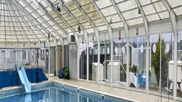 An indoor swimming pool with a glass ceiling, clear water, and a blue slide. - Heacham 2 bed Superior Caravan With Pets go Free (King's Lynn)