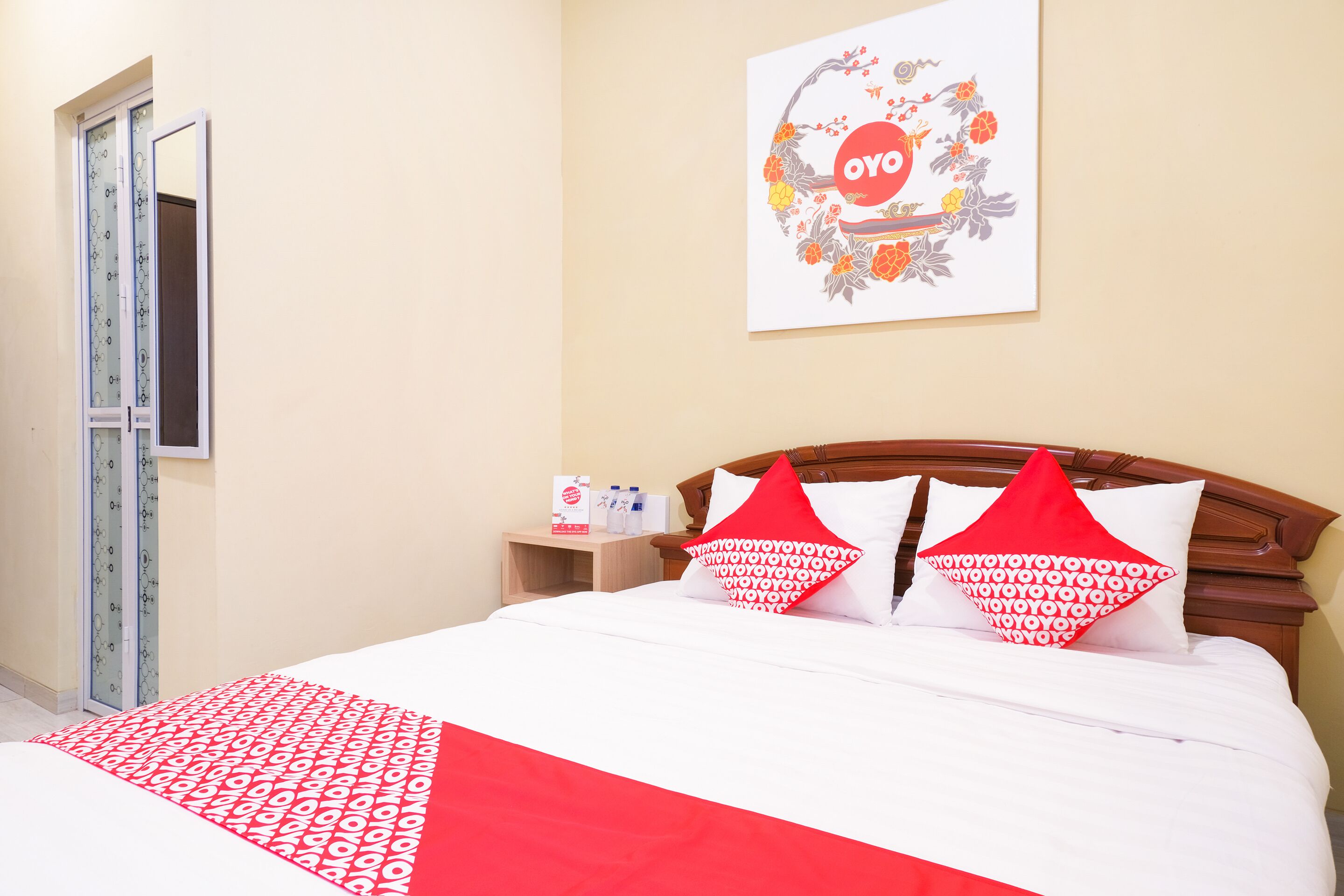 A hotel room with a bed, a wooden headboard, a nightstand with toiletries, and a framed artwork on the wall.