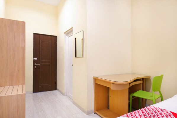 Una habitación con un armario de madera, una puerta, un espejo, un escritorio con una silla y una cama con colcha estampada.