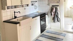 Une cuisine avec des meubles blancs, un plan de travail noir, une cuisinière et un étendoir suspendu où sont accrochés des torchons.