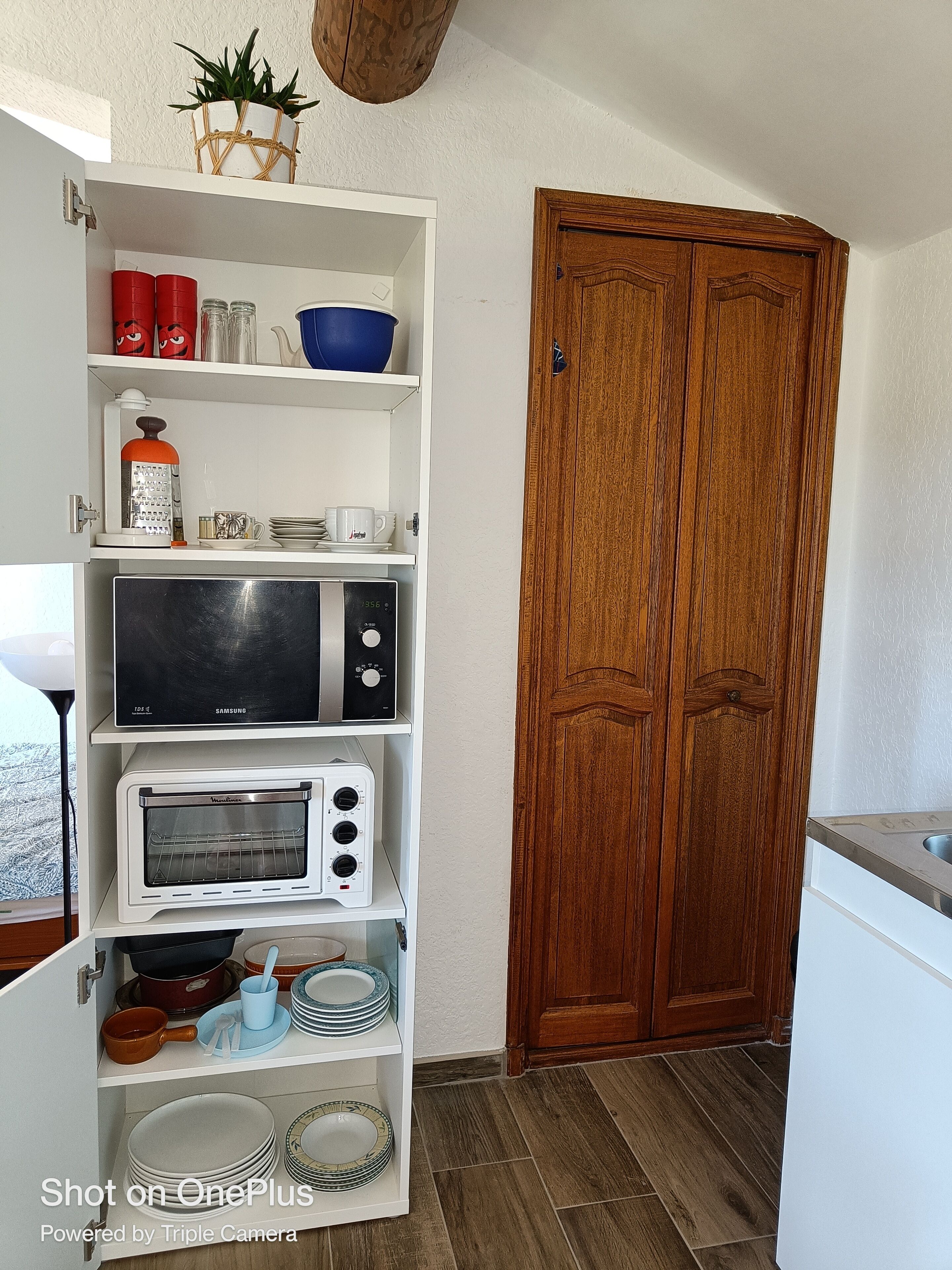 A compact kitchen with a microwave, toaster, and shelves containing dishes and kitchenware.