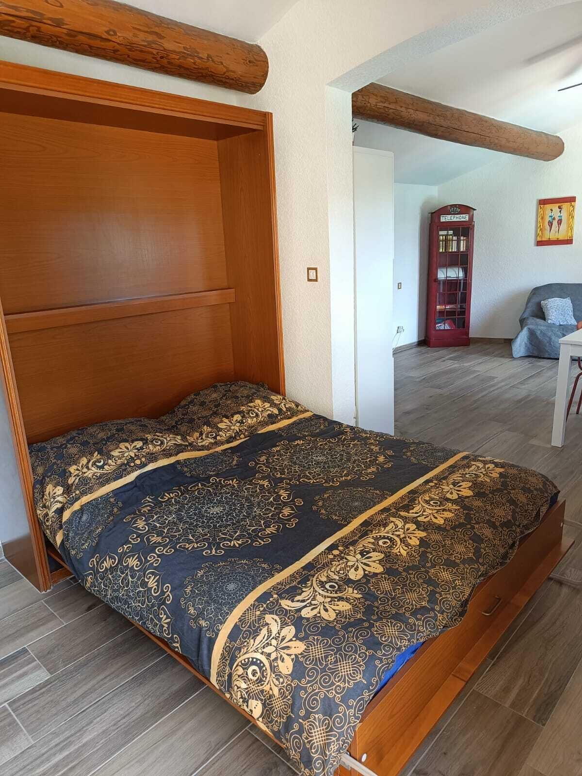 Een slaapkamer met een houten bedframe, een bed met een opvallend patroon, een rode telefooncel en een grijze bank.