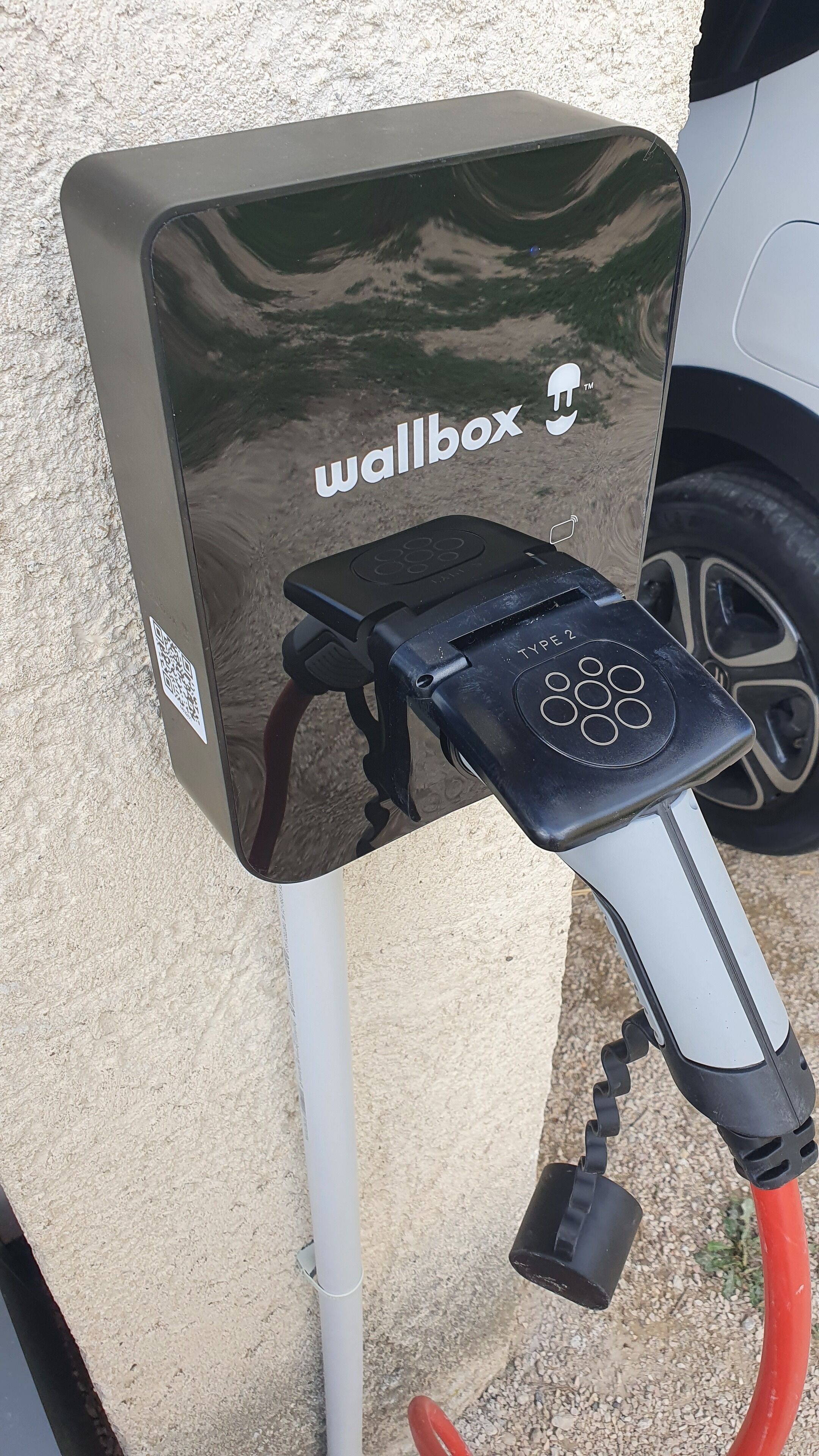 Une borne de recharge dotée d’un code QR et du logo de la marque, reliée à un câble de recharge.