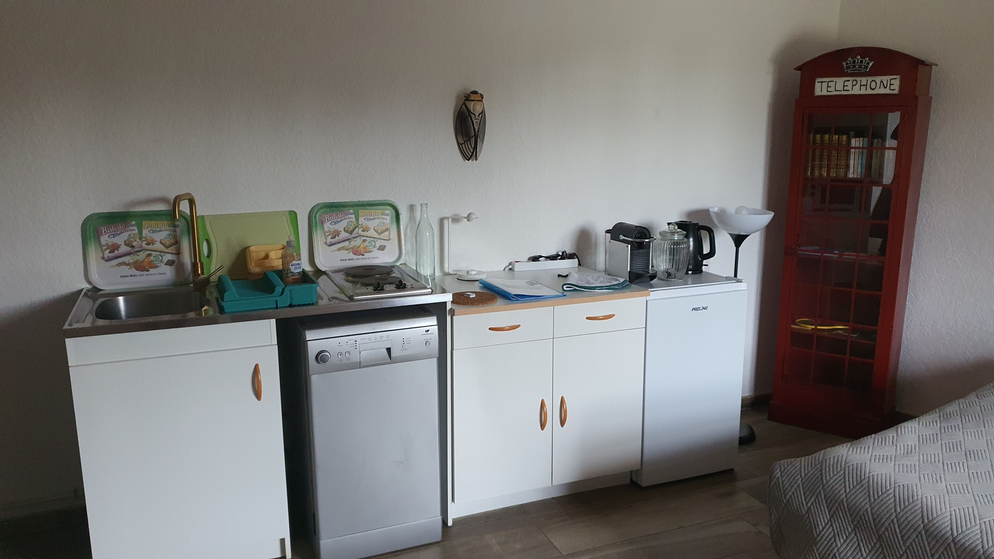Eine kleine Küchenzeile mit Spüle, Kaffeemaschine und einer roten Telefonzelle.