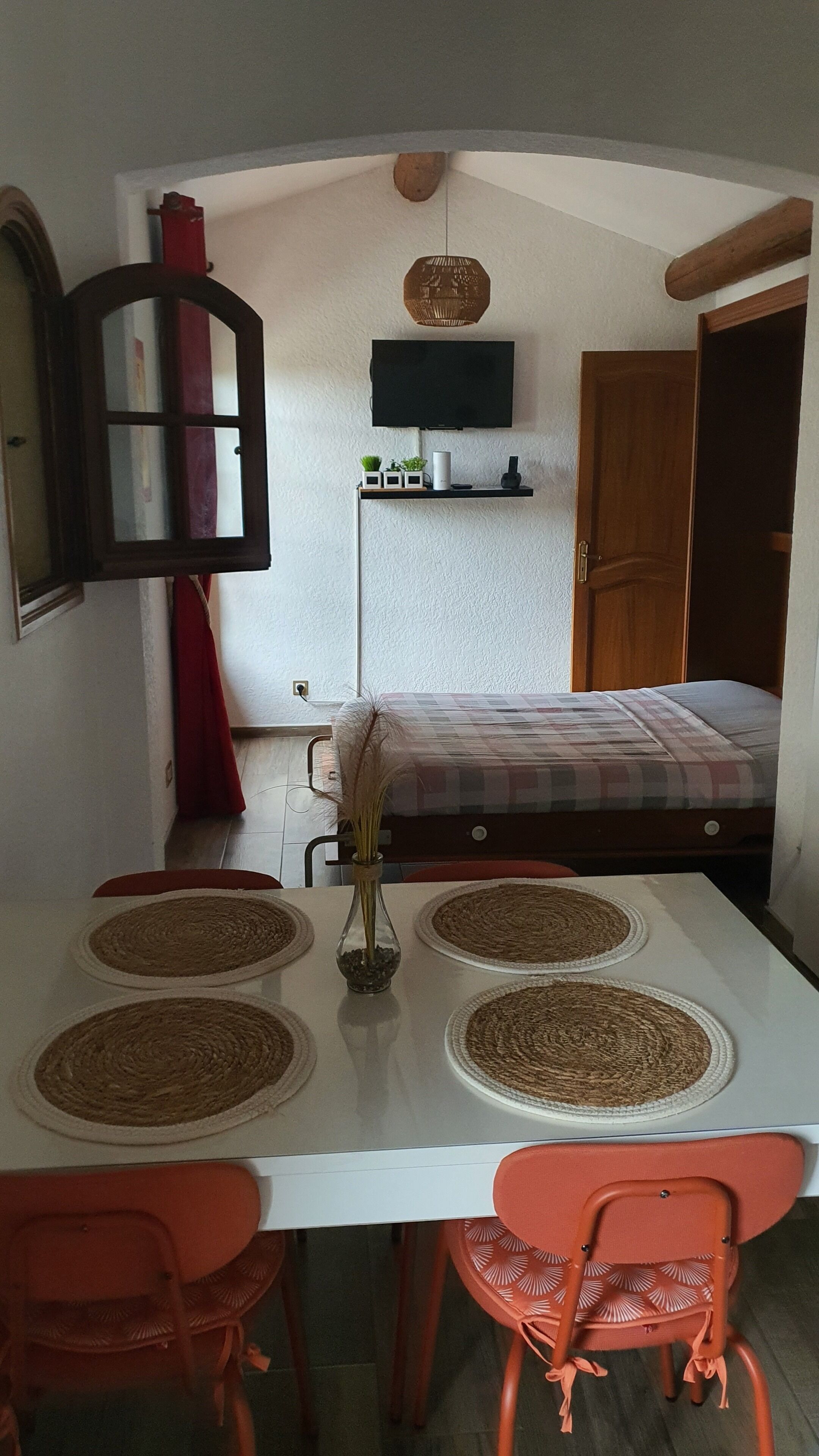 Una stanza compatta con un letto, una TV a muro, un tavolo da pranzo con sedie e un tavolino con un vaso.