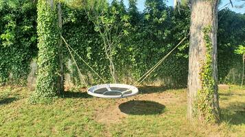 Un columpio circular con cuerdas, rodeado de árboles y césped.