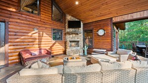 Ein Blockhaushaus-Interieur mit Kamin aus Stein, Korbmöbeln und einer Holzbalkendecke.