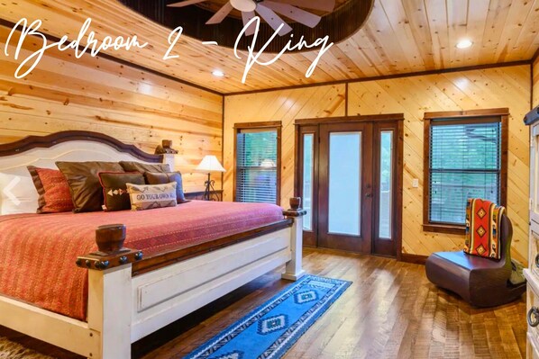 A bedroom with a wooden ceiling, a bed with pillows, a nightstand, and a window with blinds. - Southwestern Forest Retreat for Families & Friends (Broken Bow)