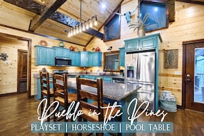 A rustic kitchen with wooden cabinets, a stainless steel refrigerator, and a large island with a pool table.