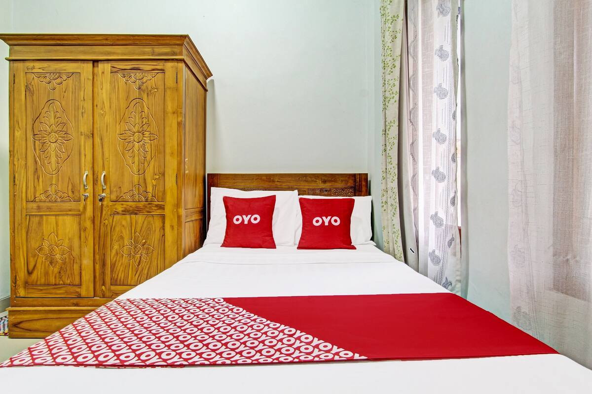 A bedroom with a wooden wardrobe, two pillows with the word "OYO" on them, and a patterned bedspread.