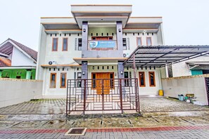 A two-story building with a signboard, a gated entrance, and a covered area with a metal roof. - Hotel O Yusman Homestay Syariah (Temon)