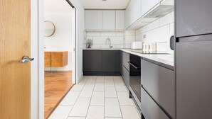 A modern kitchen with white cabinets, a black refrigerator, and a wooden floor. - Luxurious Apartment in Wandsworth (London)