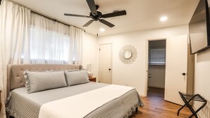 Une chambre à coucher avec un lit, un ventilateur de plafond et une porte donnant sur une autre pièce.