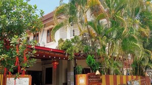 A two-story building with a red-tiled roof, surrounded by lush greenery and palm trees. - Luang Prabang Hostel (Luang Prabang)