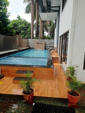 A swimming pool with a wooden deck, potted plants, and a stone wall in the background. - Lalit Hills Resort  (Mawal)